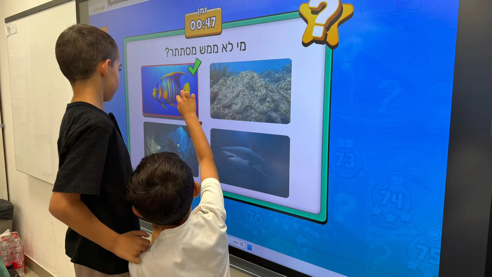 שני תלמידים בגילאים שונים פותרים יחד חידה של NickAcademy על לוח כיתתי